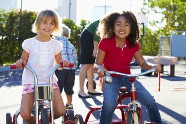 Two Girls Riding Tricycles In Playground