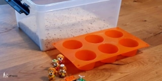 A box with rice, six small toys and a muffin tray on a table