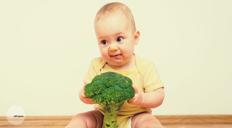 A baby holding broccoli and not looking happy