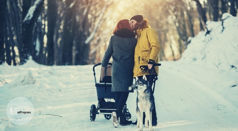 A couple with a stroller and a dog kissing in the winter outside