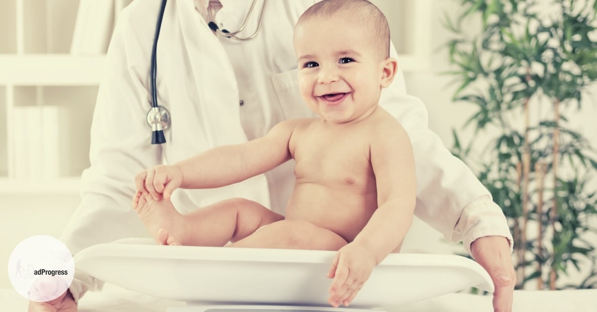 Best baby scale featured image- smiling baby on a n infant weigh and a doctor (face not showing) standing behind him