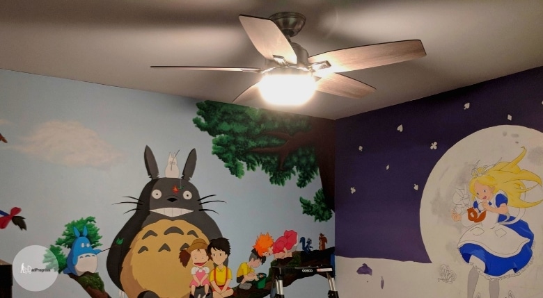 A nursery with a fan and there are cartoon characters painted on the walls (floor is not seen)