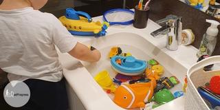 toddler standing before a sink which is filled with water and different toys