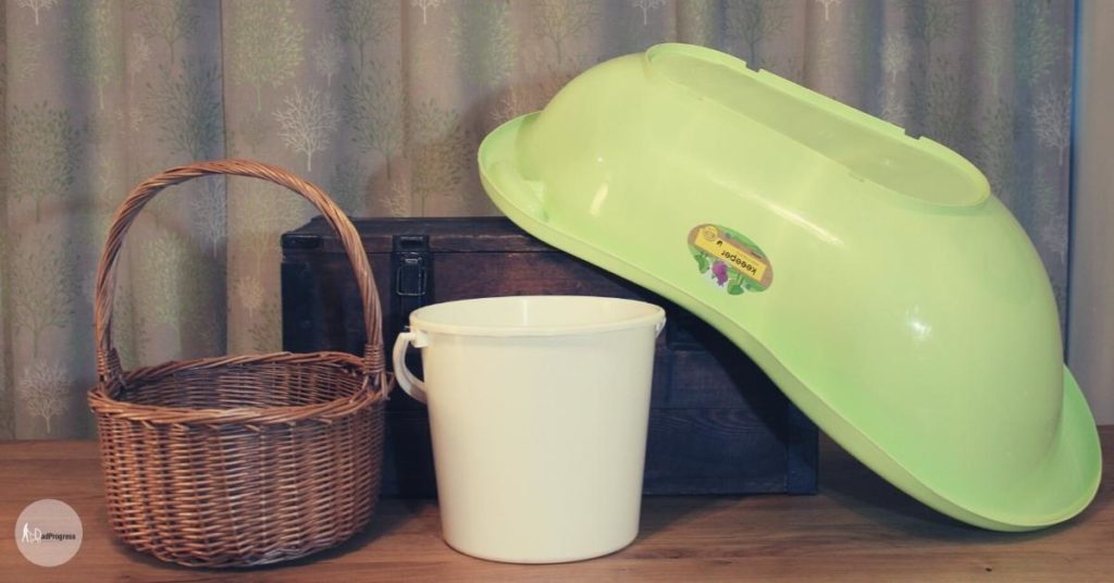 New dad survival kit vessel examples- a baby bathtub, a basket, a white bucket, a large brown wooden box with locks-on a wooden table