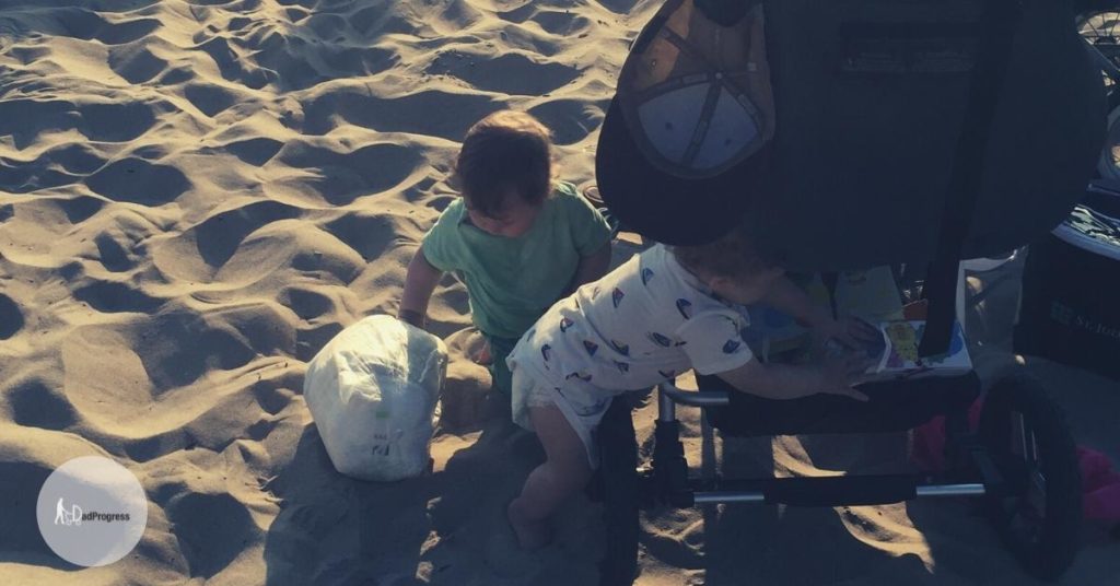 Two toddlers taking stuff out from a stroller on sand