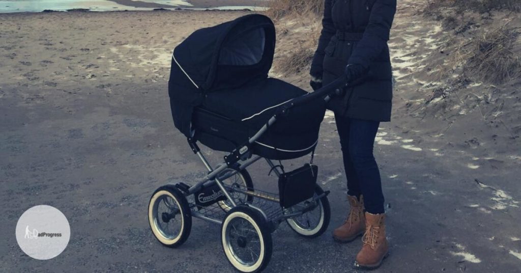 Traditional stroller (pram) on frozen sand and a woman standing next to it