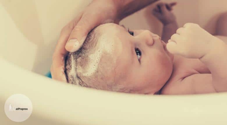 Baby in a bathtub and a hand washes the hair