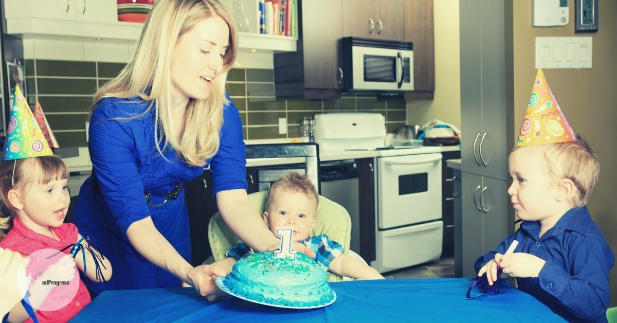 First Birthday gifts from grandparents featured image- one year old sitting behind a table between two toddlers and mother presenting him a blue cake