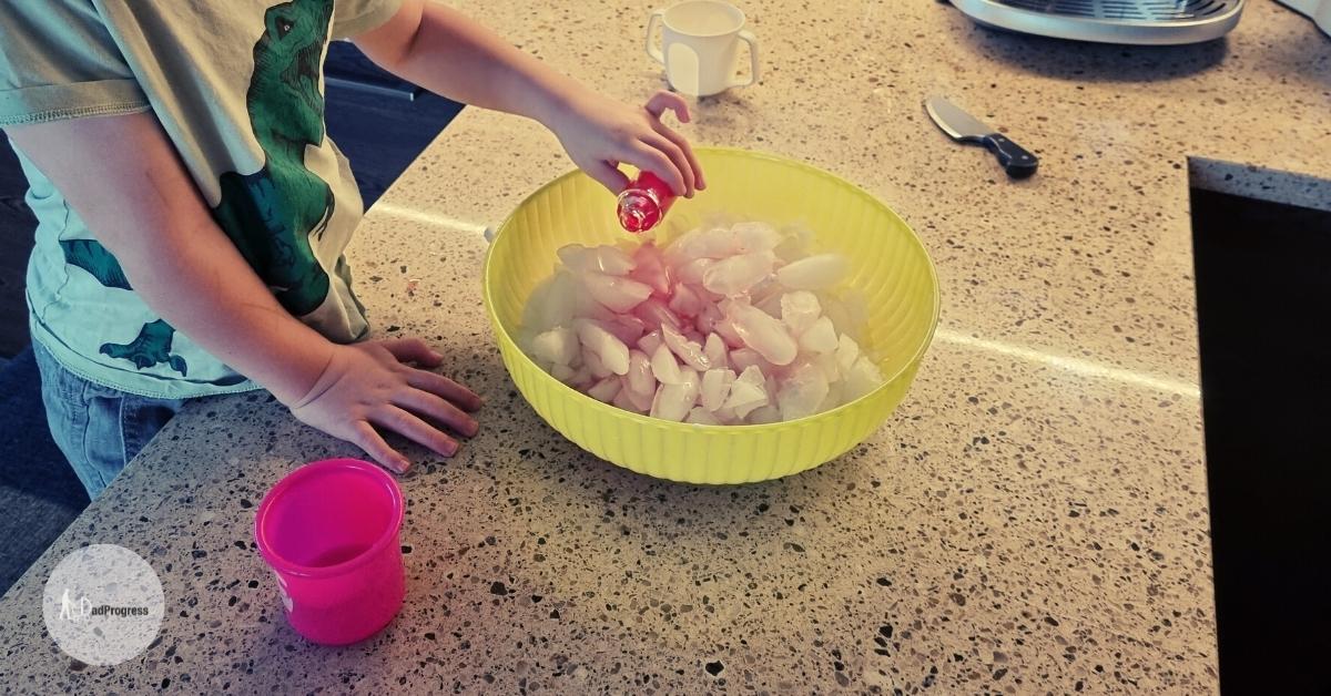 Fizzing ice cubes activity- hand of a toddler pours vinegar on the ice