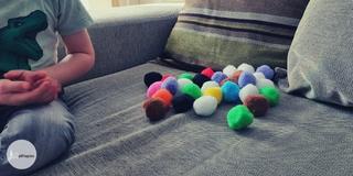 Pop-poms on a sofa and a toddler sitting next to them (face not seen)